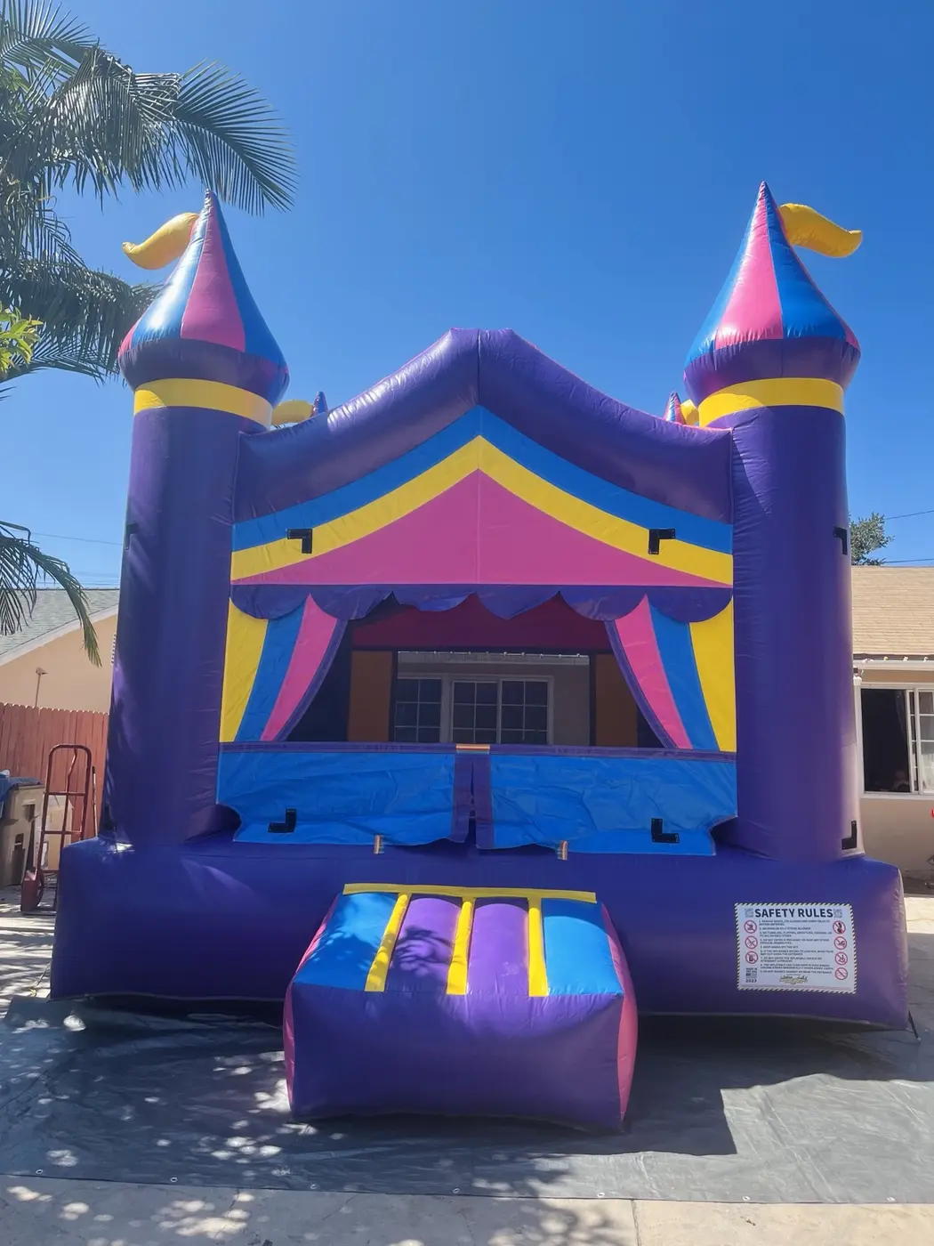 Purple, blue, pink and yellow castle bounce house viewed from the front