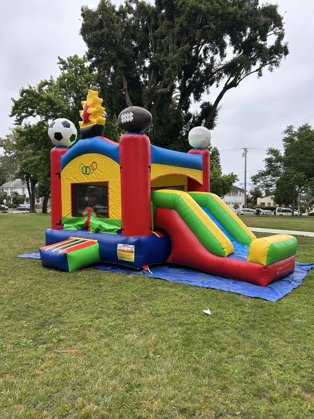 Sports-themed bounce house with a large side slide set up in a park