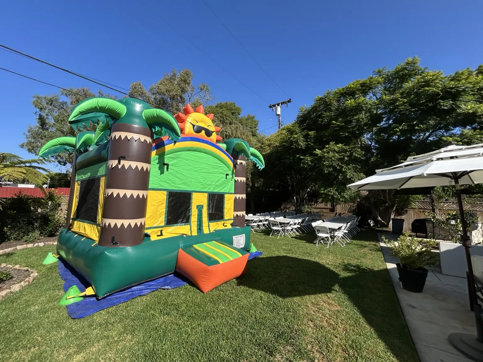 Tropical bounce house set up on a lawn beside party tables and chairs